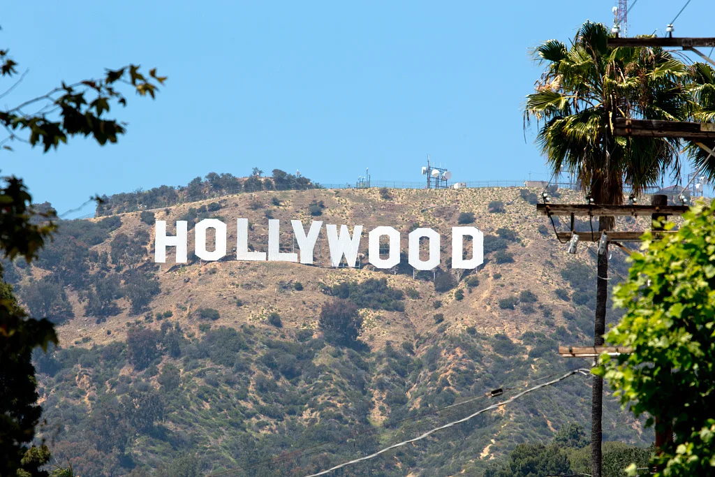Hollywood ցուցանակը բլրի լանջին՝ ծառերի միջև, կապույտ երկնքի տակ